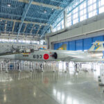 Airpark JASDF Hamamatsu Air Base Museum (航空自衛隊 浜松広報館) A silver fighter jet with the number 693 and Japanese markings is displayed inside the spacious, modern Airpark Hamamatsu museum hangar with blue steel beams and large windows, surrounded by white railings.
