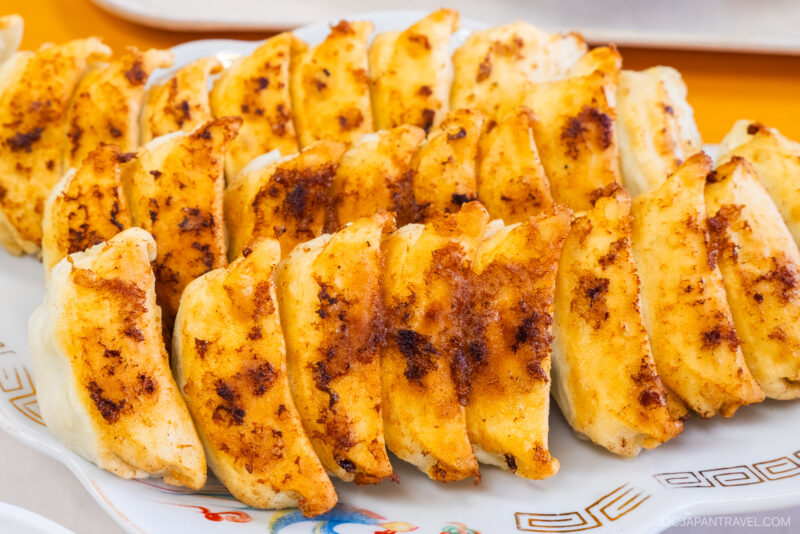 A close-up of a plate filled with neatly arranged, golden-brown Hamamatsu Gyoza (pan-fried dumplings) with crispy edges, ready to be served.