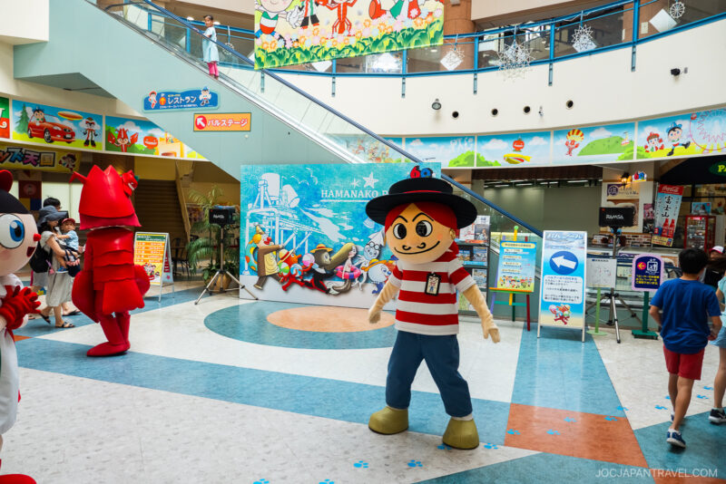 A person in a large cartoon pirate mascot costume stands indoors at Hamanako Pal Pal, a colorful amusement center, with other mascots and people nearby. Bright decorations and signage are visible in the background.