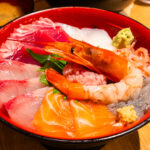 Seafood in Numazu (沼津) – Fresh Catches from Suruga Bay A colorful bowl of assorted sashimi, featuring shrimp, salmon, tuna, and other raw fish slices served on rice and garnished with wasabi and ginger—a true Numazu specialty. Miso soup is in the background.