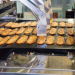 Unagi Pie Factory Tour (うなぎパイファクトリー) – Hamamatsu’s Quirky Snack Tour Rows of rectangular cookies move along a conveyor belt in the Unagi Pie Factory, passing under a metal mechanism during the production process.