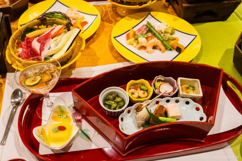 A colorful Japanese kaiseki meal at Jozankei Onsen features assorted small dishes, vegetables, seafood, and desserts arranged neatly on trays and plates, showcasing elegant presentation and vibrant ingredients.