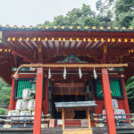 Kunozan Toshogu Shrine (久能山東照宮) – Legacy of Tokugawa Ieyasu A traditional Japanese shrine, Kunozan Toshogu Shrine features a red wooden structure, ornate roof, green shutters, and decorative barrels, all surrounded by lush greenery.