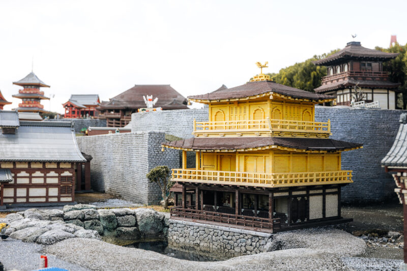 A detailed miniature model of a traditional Japanese temple with yellow-golden walls and a tiered roof, inspired by Nagoya architecture, is surrounded by stone walls and set near a pond—perfect for any Legoland Nagoya travel guide.