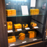 Sekisho Karakuri Museum (箱根関所からくり美術館) – Puzzle Boxes and Yosegi Craft in Hakone A glass display case at the Sekisho Karakuri Museum showcases various wooden puzzle boxes with intricate geometric and traditional designs, each placed on shelves with small white labels in front of them.