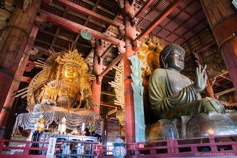 The large bronze Buddha statue and ornate golden statue inside Todaiji Temple in Nara, Japan, are surrounded by wooden pillars and intricate architectural details.