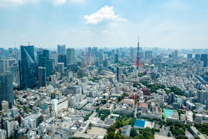 Aerial view of Tokyo’s cityscape with dense high-rise buildings, the iconic Tokyo Tower in the distance, and a hazy sky overhead captures a stunning tokyo city view.
