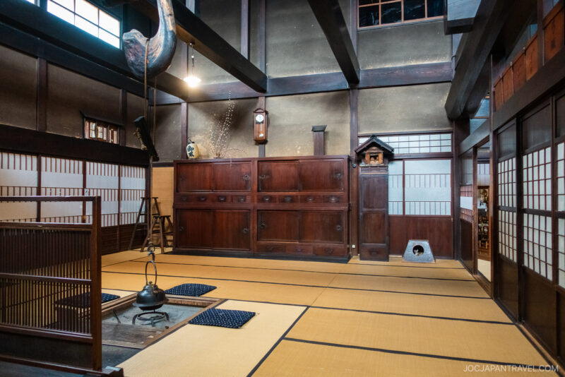 Traditional Japanese room with tatami mats, wooden cabinets, shoji screens, and a suspended kettle over a hearth, inspired by Kusakabe Heritage House, creating a serene and authentic atmosphere with minimal décor.