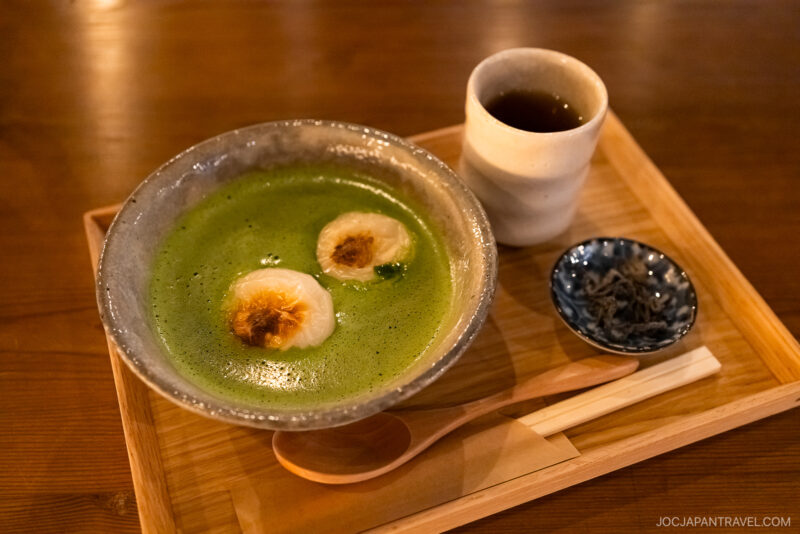 A bowl of matcha green tea with toasted marshmallows, served on a wooden tray alongside tea, pickles, a spoon, and chopsticks—a must-try Kyoto what to eat experience.