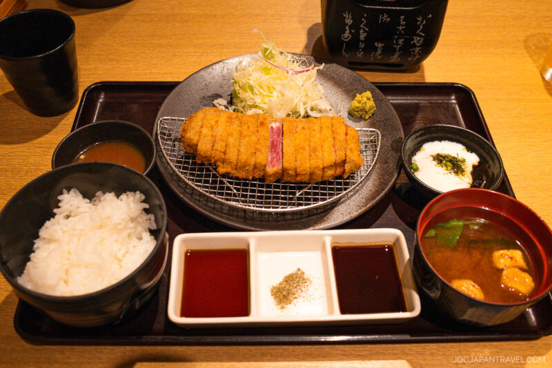 A Japanese meal set—perfect for those wondering kyoto what to eat—featuring breaded pork cutlet, shredded cabbage, white rice, miso soup, dipping sauces, and pickles, all neatly arranged on a tray.