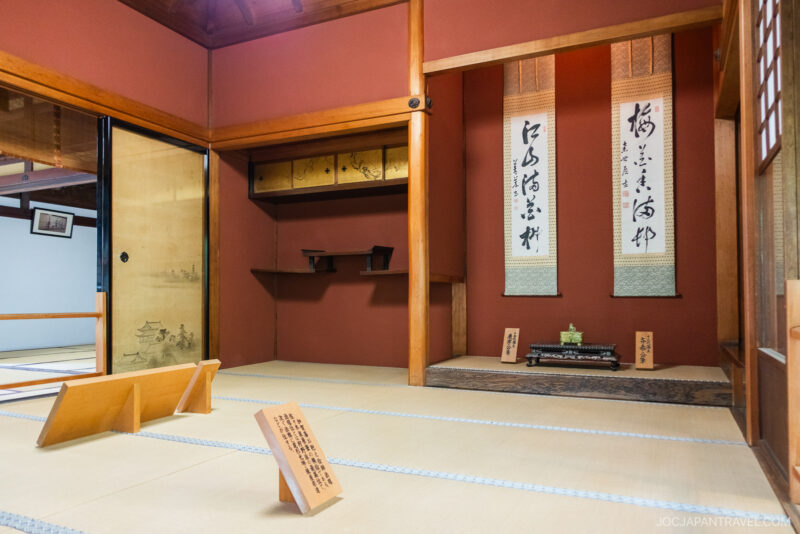 Traditional Japanese tea room with tatami mats, sliding doors, and wooden beams evokes the serenity of the Nagamachi Samurai District. Artistic scrolls in an alcove, low benches, and placards complete this calm, neatly arranged space.