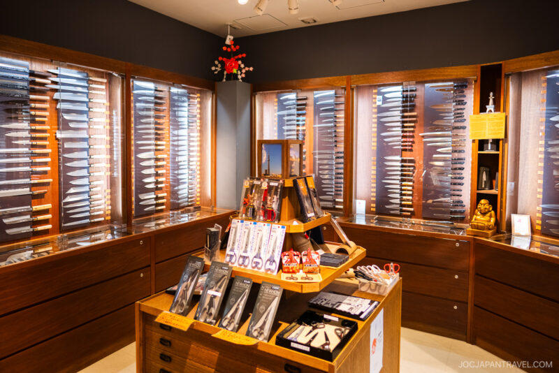 A brightly lit knife shop in Tokyo Skytree Town features wooden display cases filled with various knives. A central table showcases scissors, knives, and kitchen tools, all highlighted by spotlights for an inviting atmosphere.