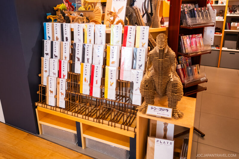 A store display in Tokyo Skytree Town features flat-pack animal and figure cardboard sculpture kits neatly arranged on shelves, with a large assembled cardboard gorilla model sitting on a smaller table to the right.