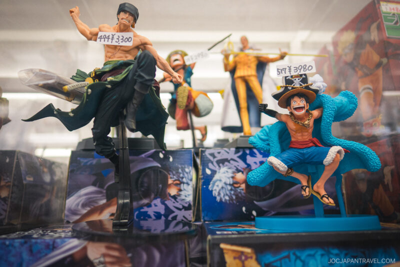 Two One Piece anime character figurines are displayed in a shop, each with a yen price tag on their heads—a common sight in Akihabara Hobby Stores, where shelves are filled with more anime figures and merchandise.
