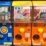 Three colorful Japanese capsule toy vending machines from Akihabara Gachapon Hall, each labeled in Japanese and displaying images of collectible toys like pouches, pens, and figurines.