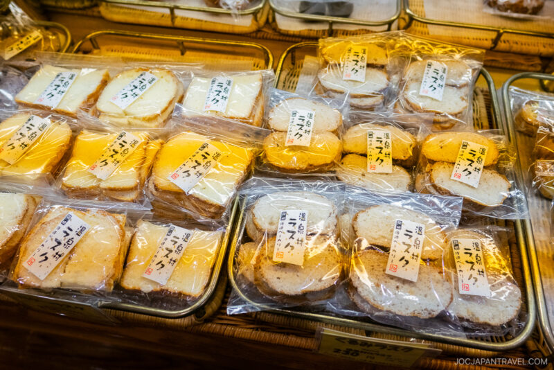 Sliced bread pieces from Hakone Watanabe Bakery, individually wrapped in clear plastic with Japanese labels, are displayed neatly in baskets at a market or bakery.