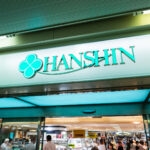 A store entrance with a sign reading HANSHIN in teal letters and a clover logo above, welcoming shoppers into the brightly lit interior—a vibrant scene at the Hankyu and Hanshin Department Stores Osaka.