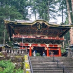 Nikkosan Rinnoji Taiyuin (日光山輪王寺大猷院) – The Resting Place of Tokugawa Iemitsu A colorful traditional Japanese temple, Nikkosan Rinnoji Taiyuin, with intricate carvings and gold details stands among tall trees. Several visitors are on the stone steps leading up to the entrance.
